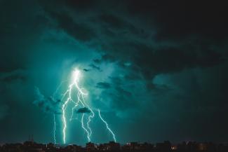 a lightning bolt striking over a city at night by Theo Tab courtesy of Unsplash.